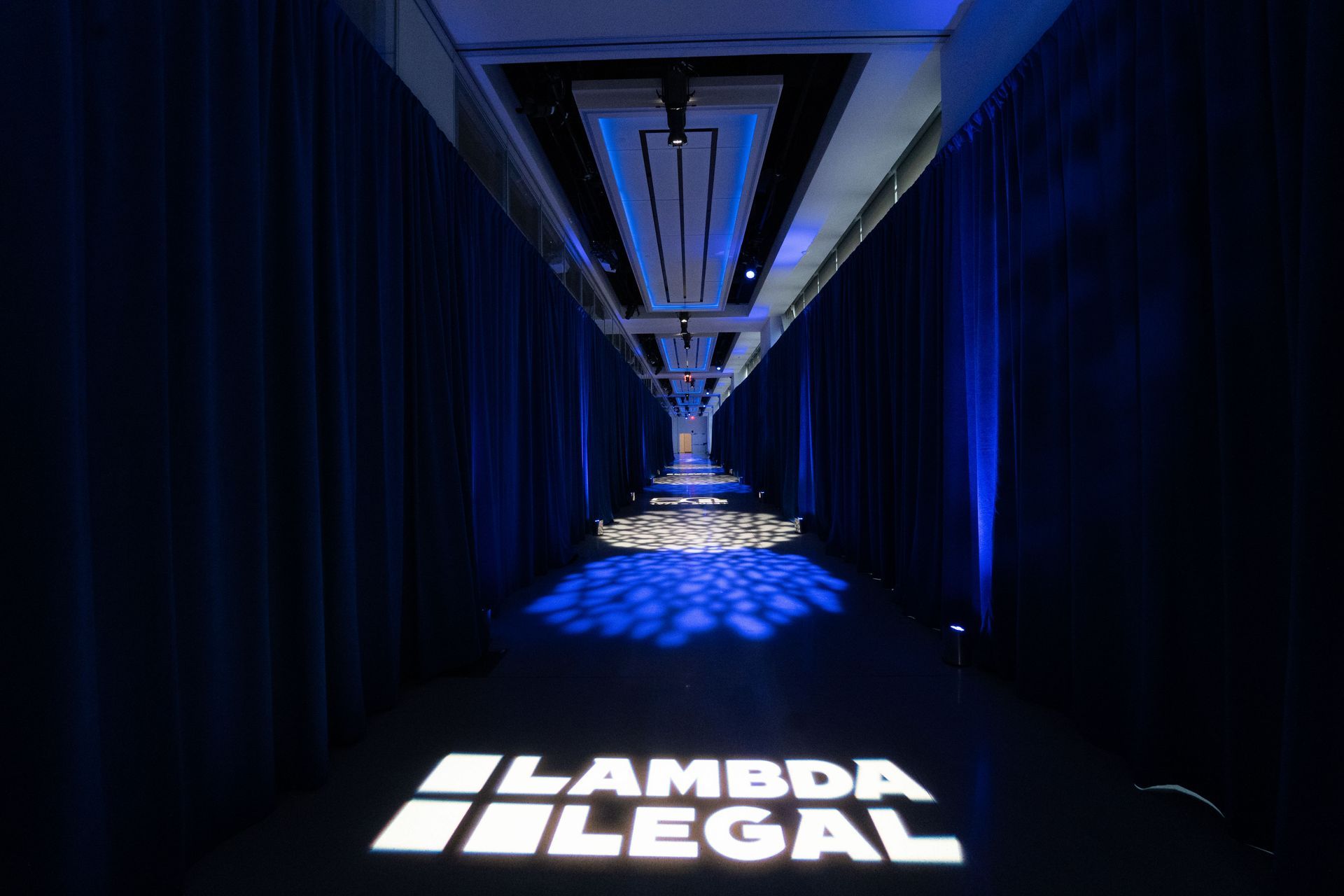 A hallway with blue curtains and a lambda legal logo on the floor.