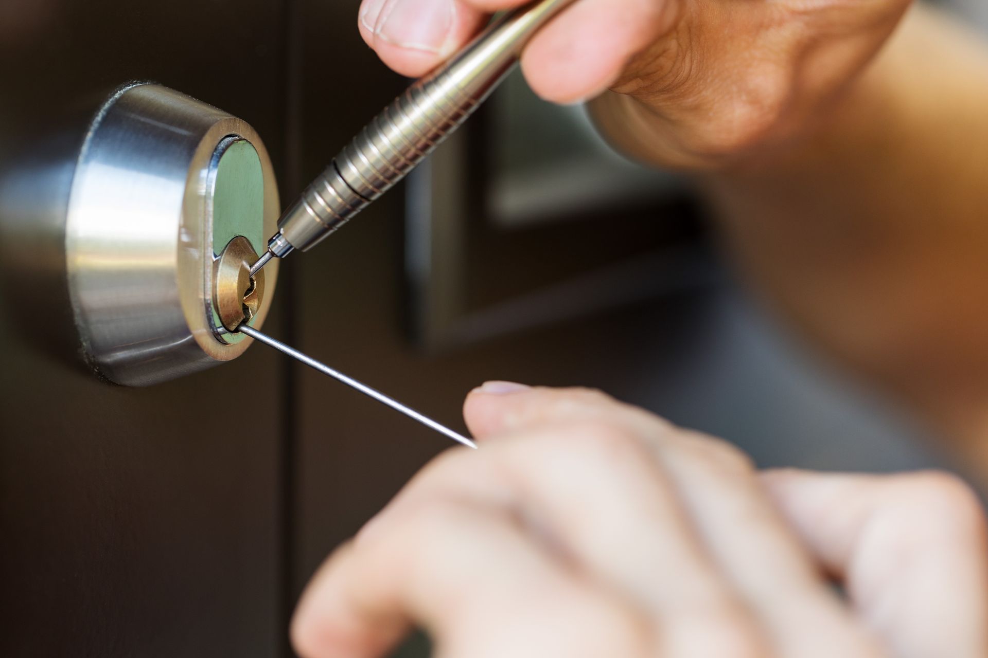 Closeup of locksmith’s hands using pick tools to open a locked door.