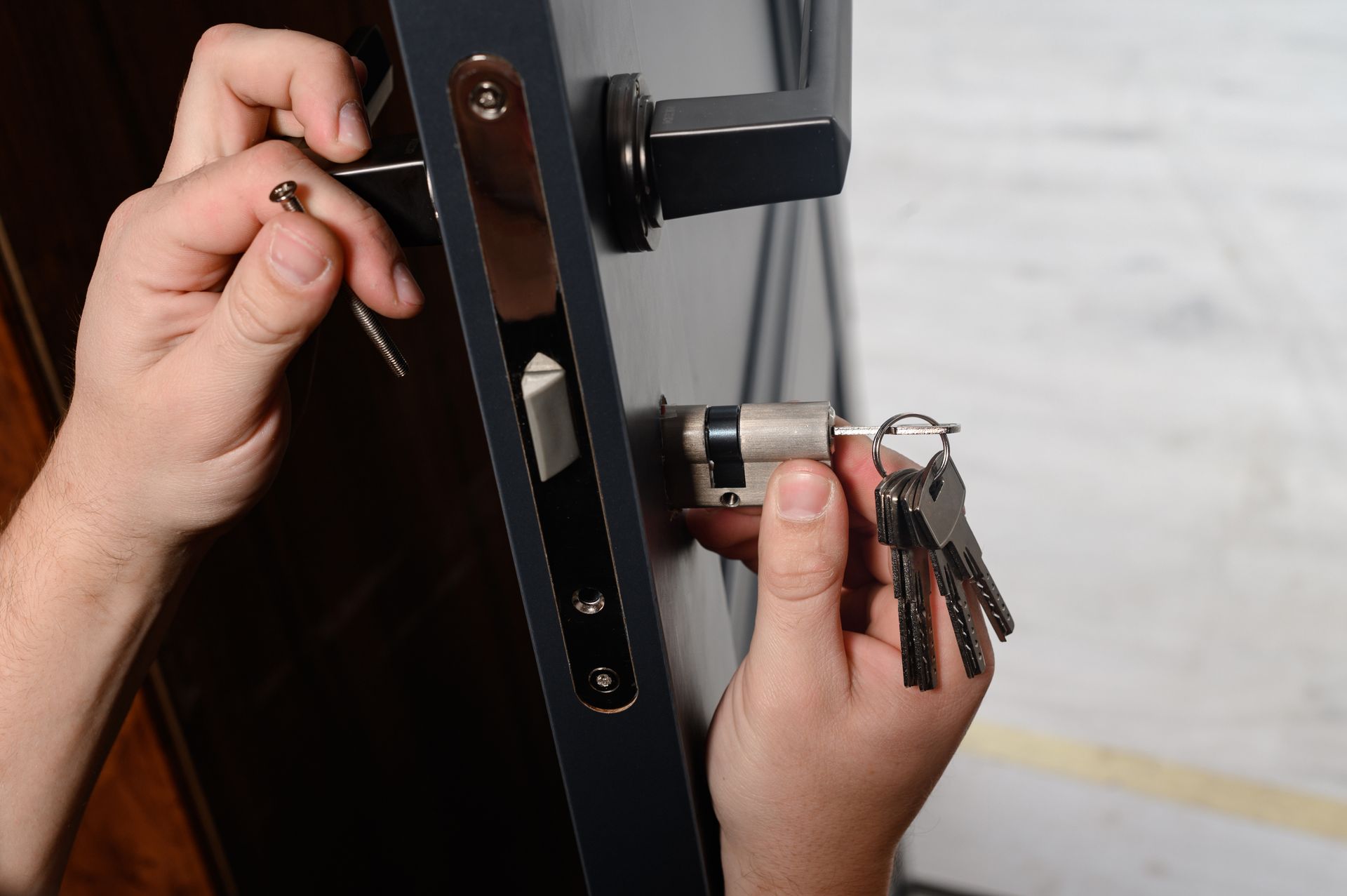Hands installing a door lock cylinder with keys and screws during door hardware replacement.