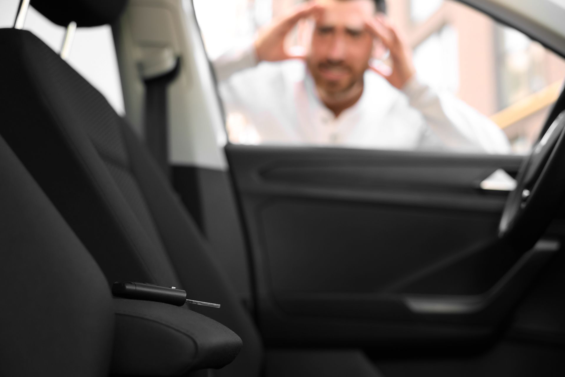 Frustrated man looking through a car window at keys locked inside the vehicle.
