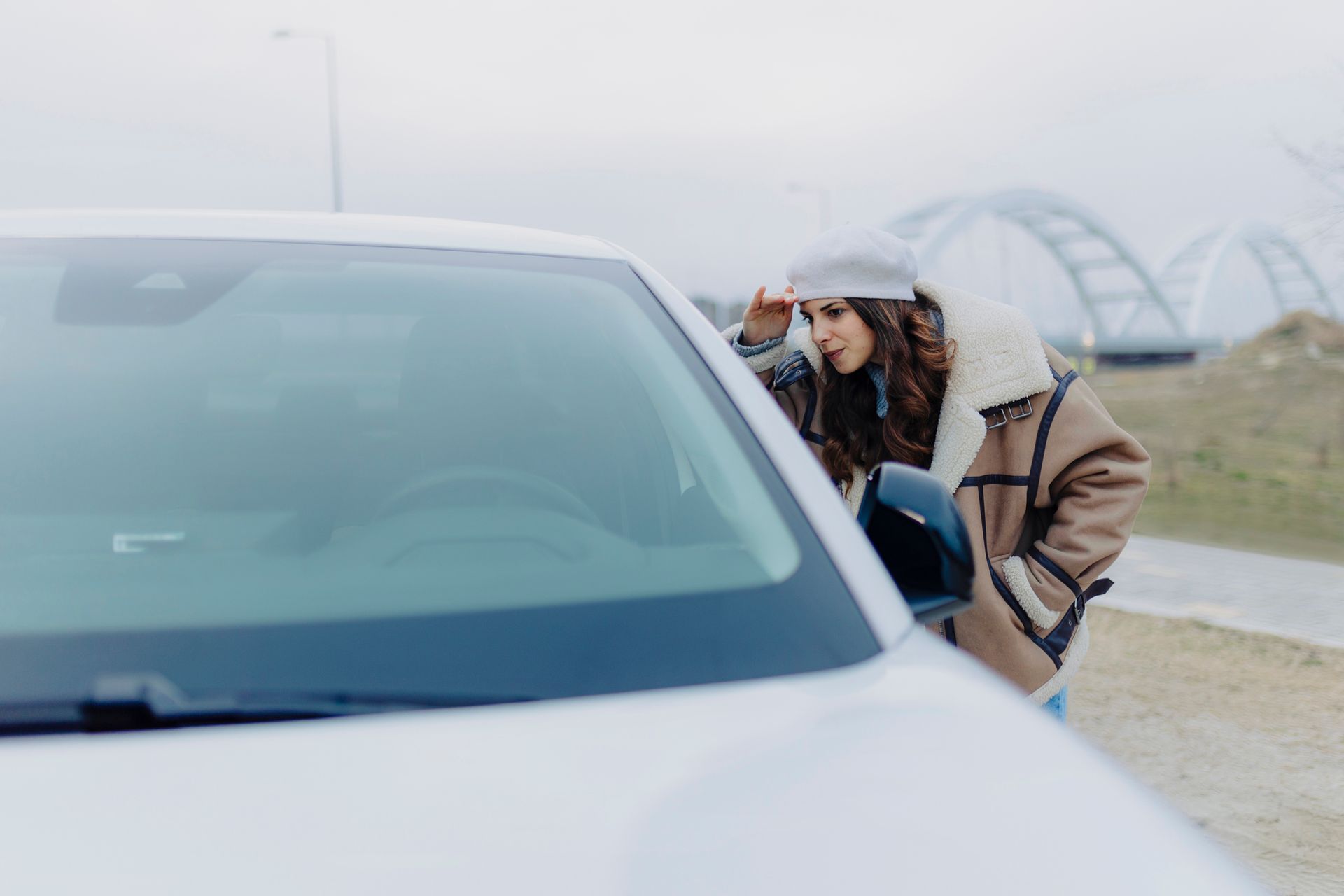 A woman stands beside a car on the road, looking worried, possibly facing a car lockout issue.