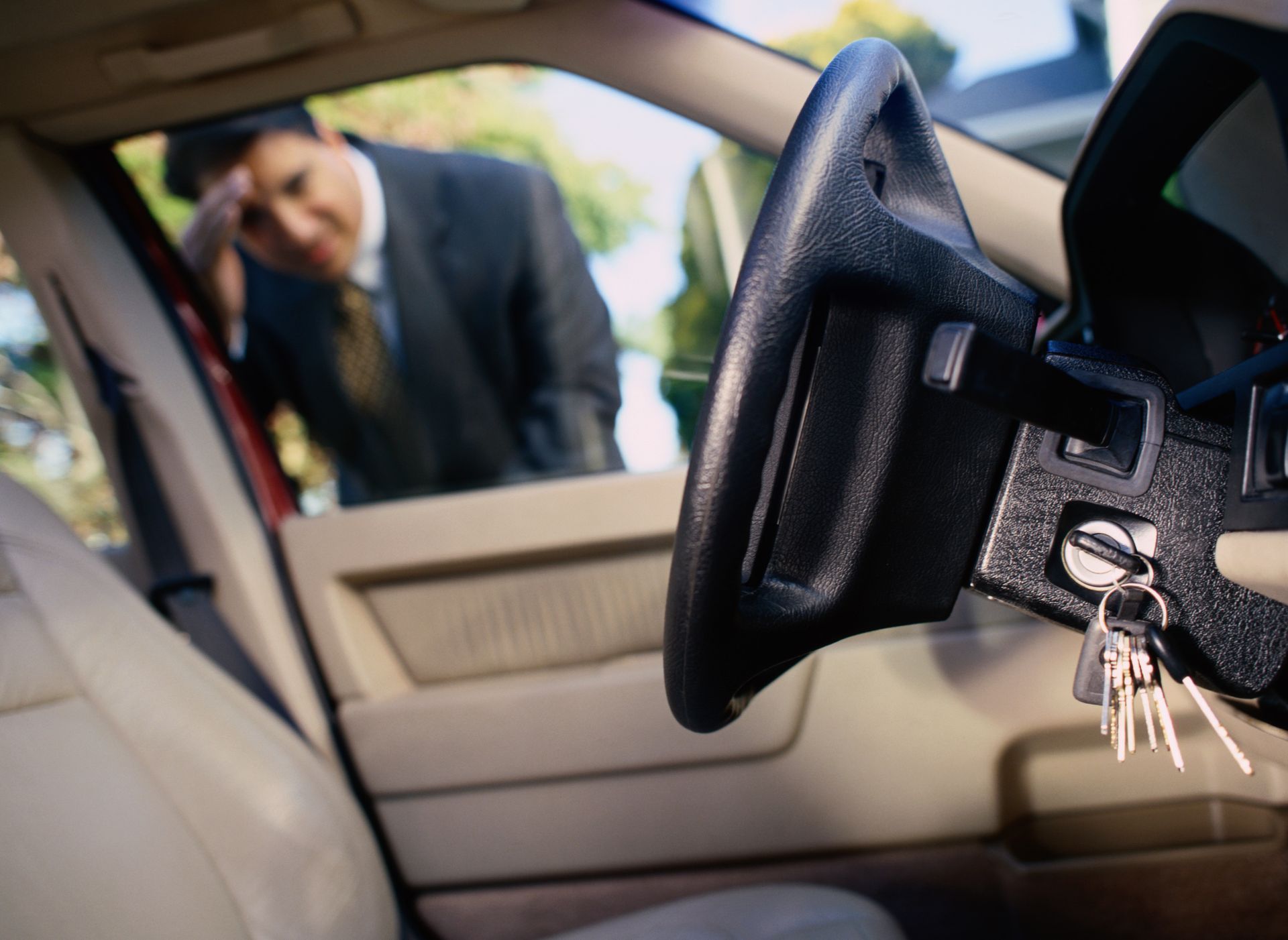 A concerned man inspects his car keys near his vehicle, possibly dealing with a car lockout.
