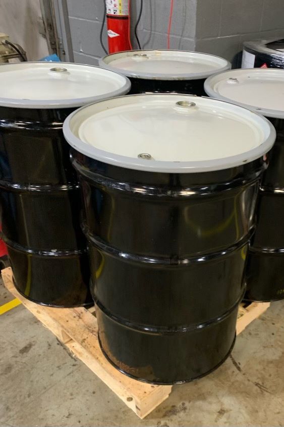 A bunch of black barrels with white lids are sitting on a wooden pallet.