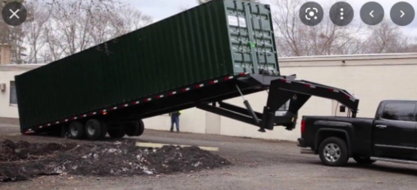 A truck is towing a green shipping container on a trailer.