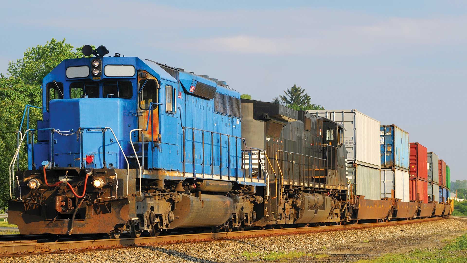 A blue train is going down the tracks carrying containers.