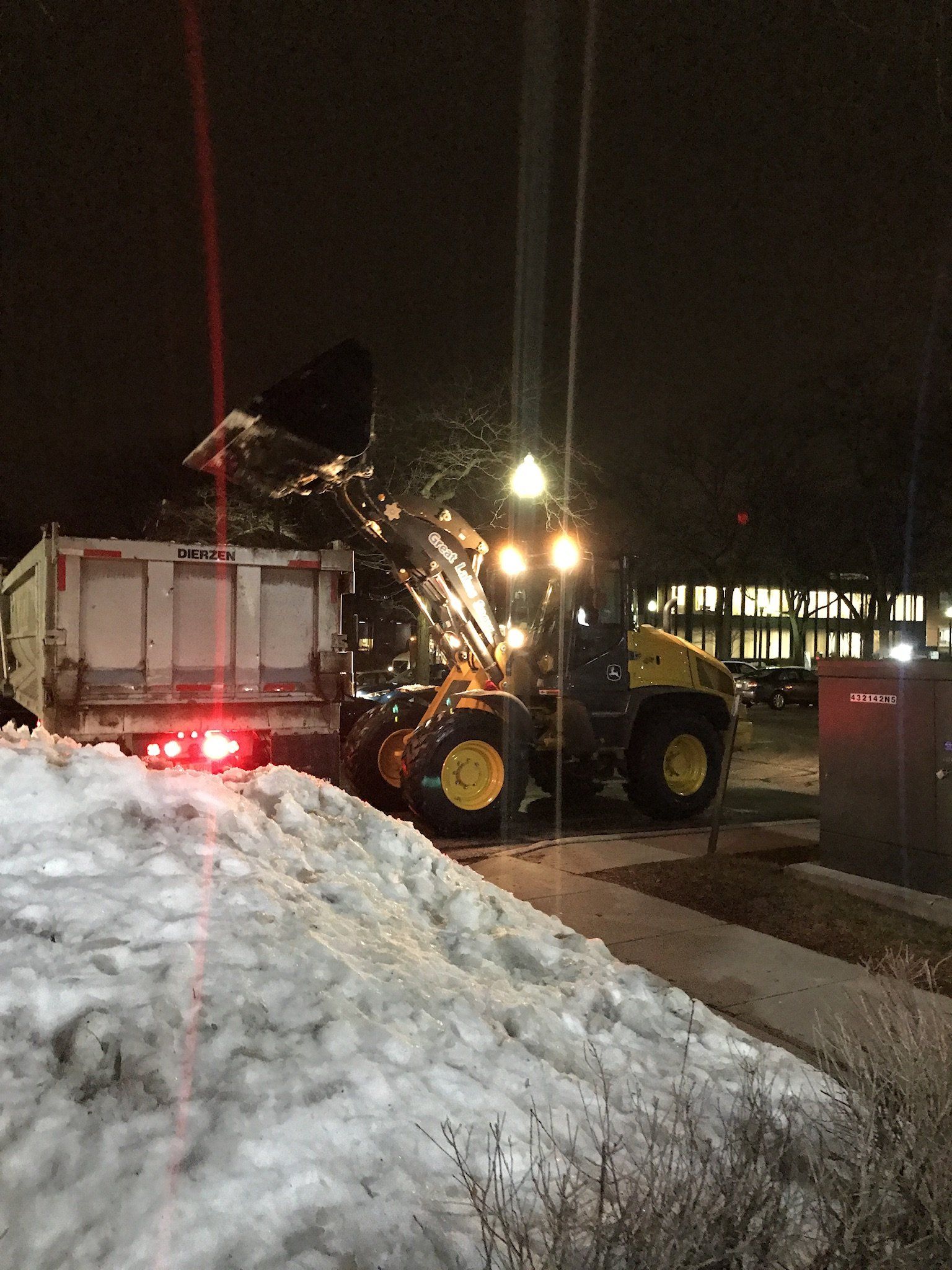 a front end loader dumping snow into a dump truck to be hauled away
