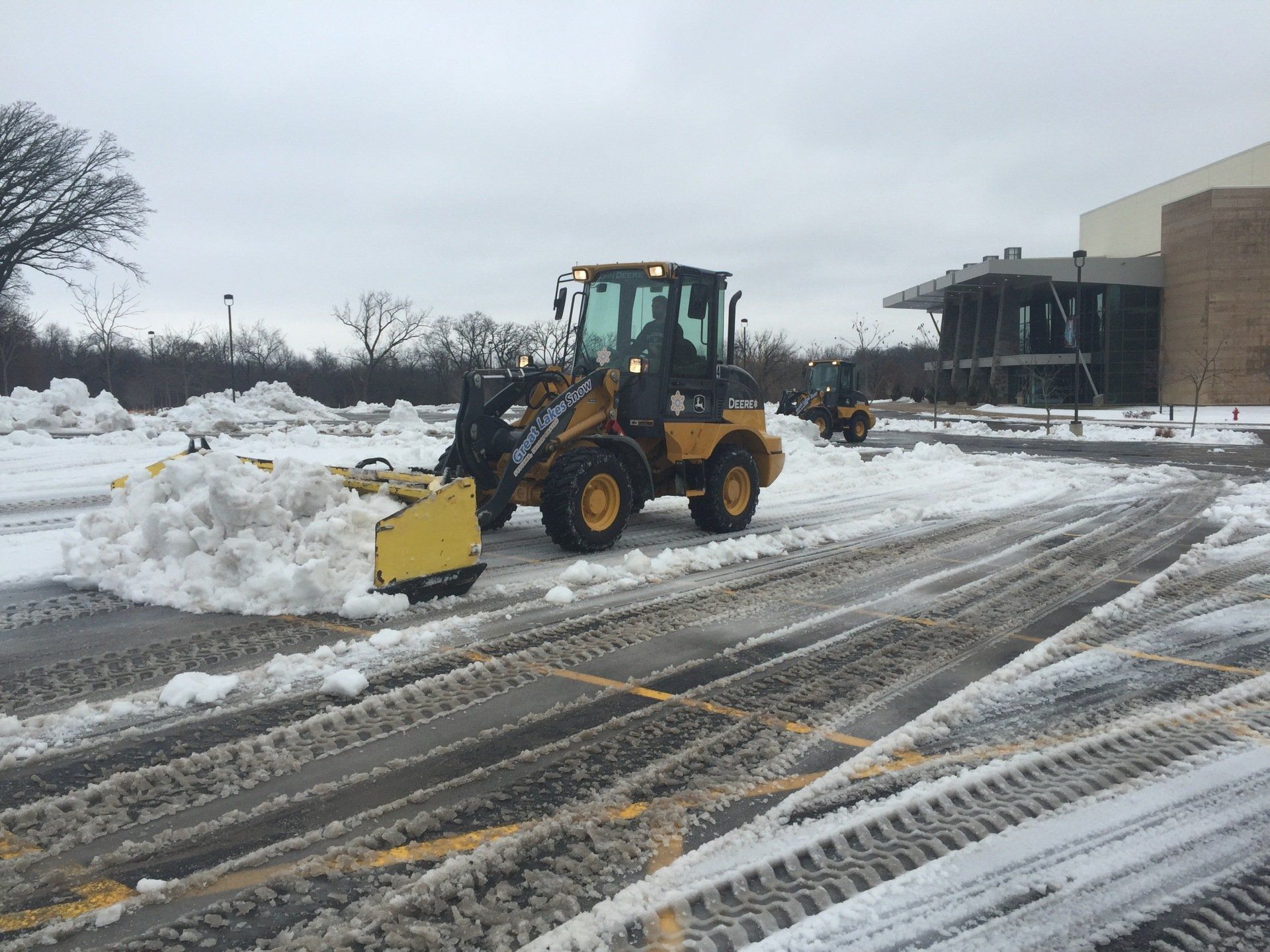 A snow plow is clearing snow from a parking lot.