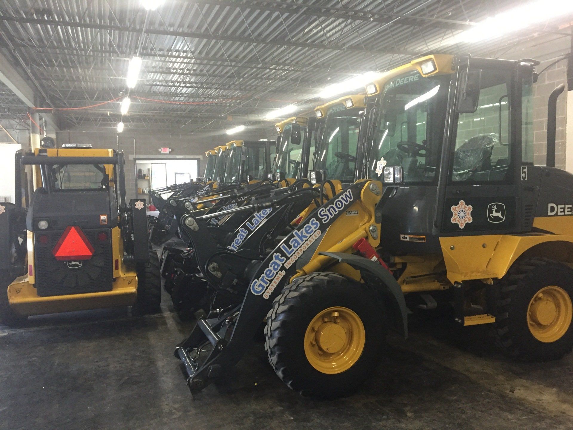 A row of yellow and black tractors are parked in a garage.