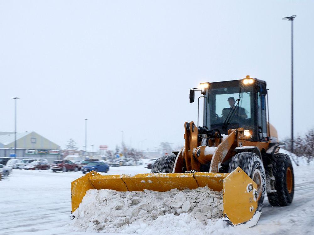 Yellow snowplow clearing a snowy parking lot near parked cars