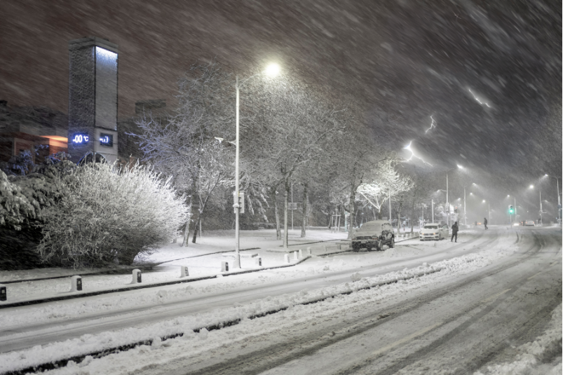 A car is driving down a snowy street at night.