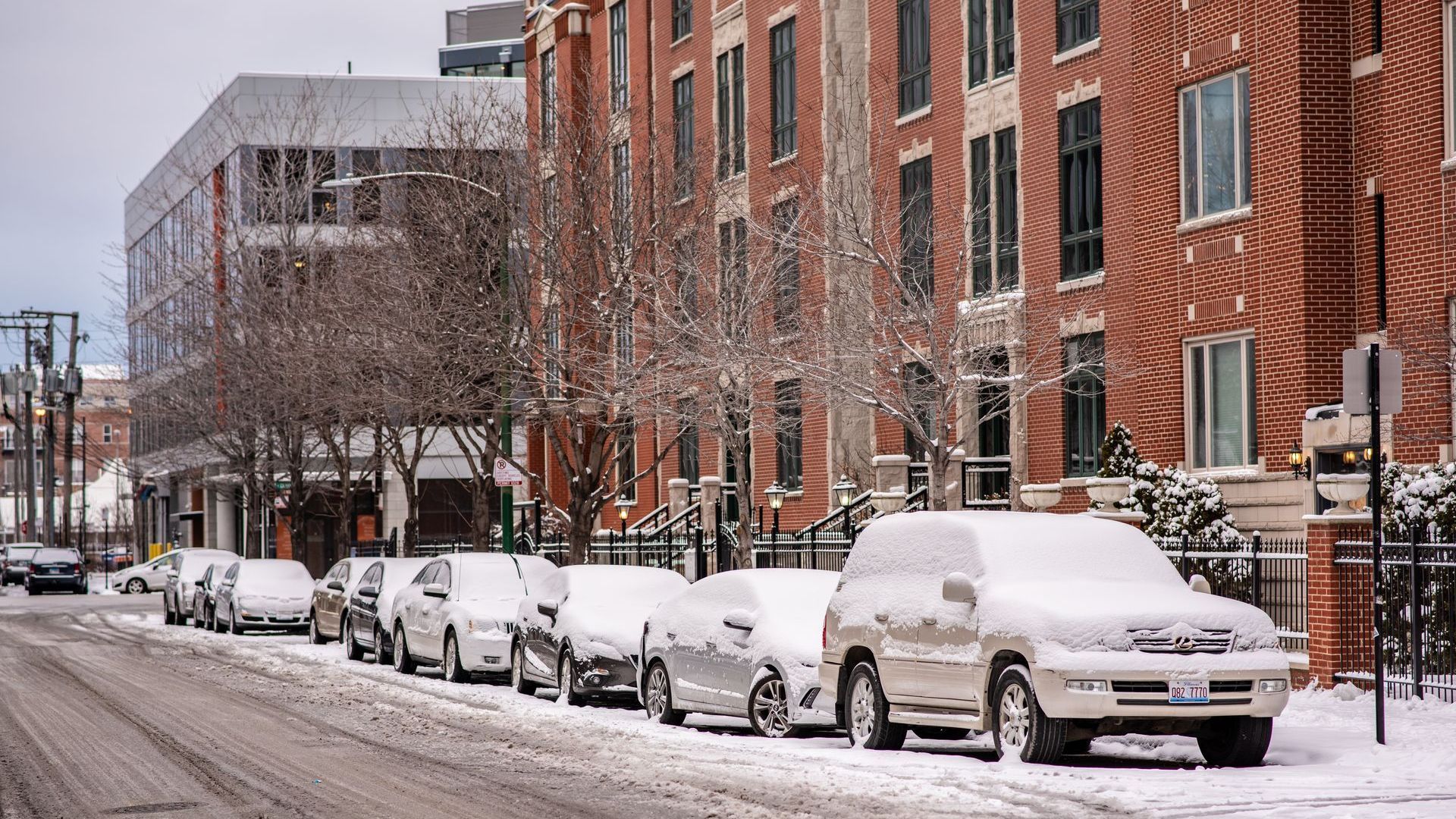 A row of cars are parked on the side of a snow covered street.