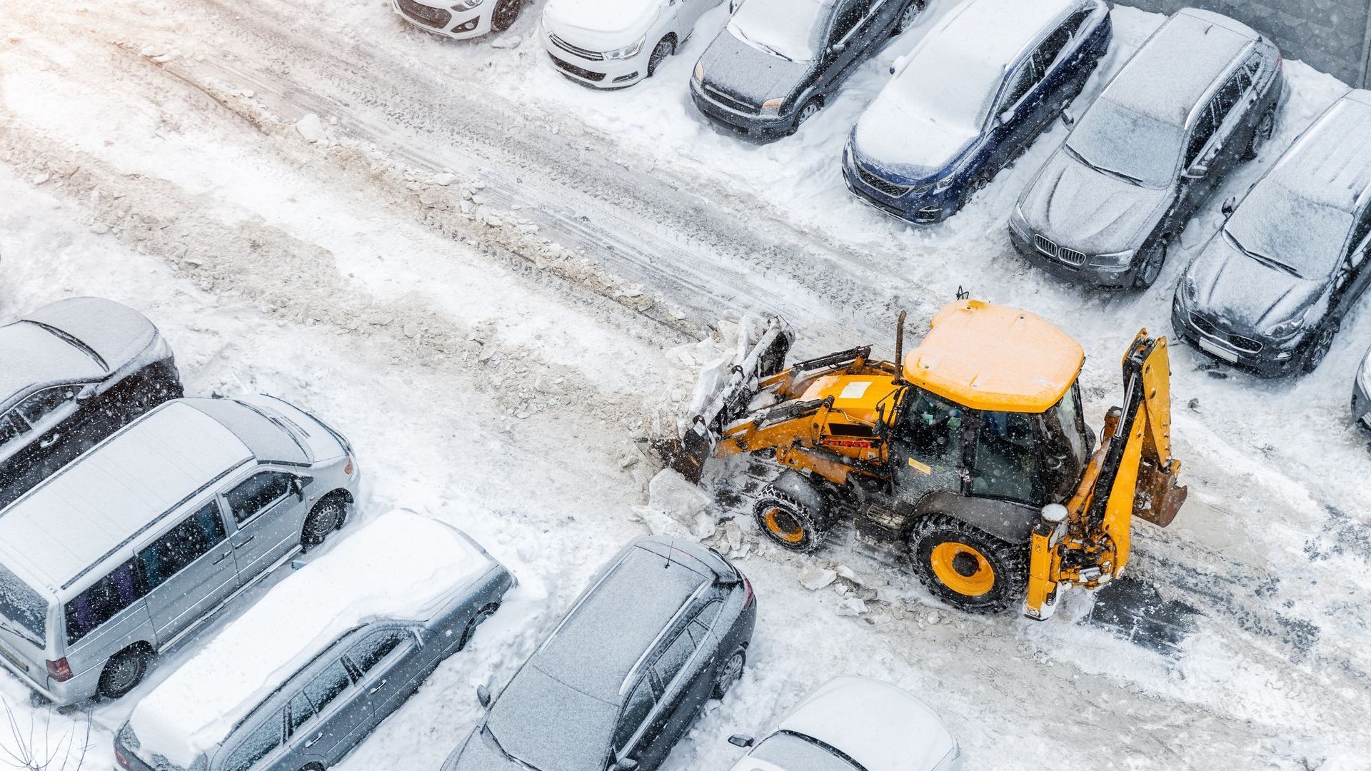 An aerial view of a snow plow clearing snow from a parking lot.
