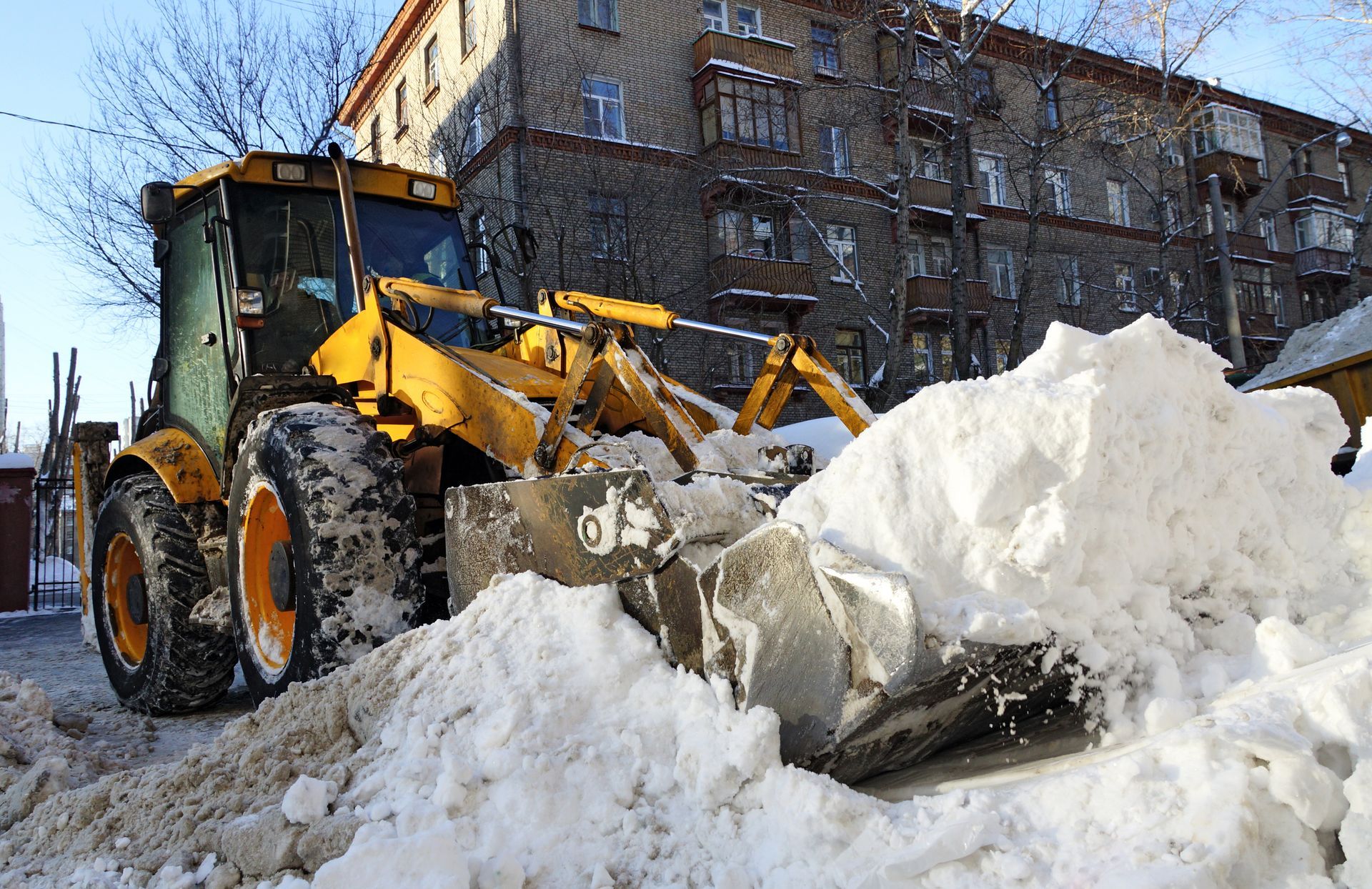 a yellow tractor is loading snow into a dump truck for commercial snow removal