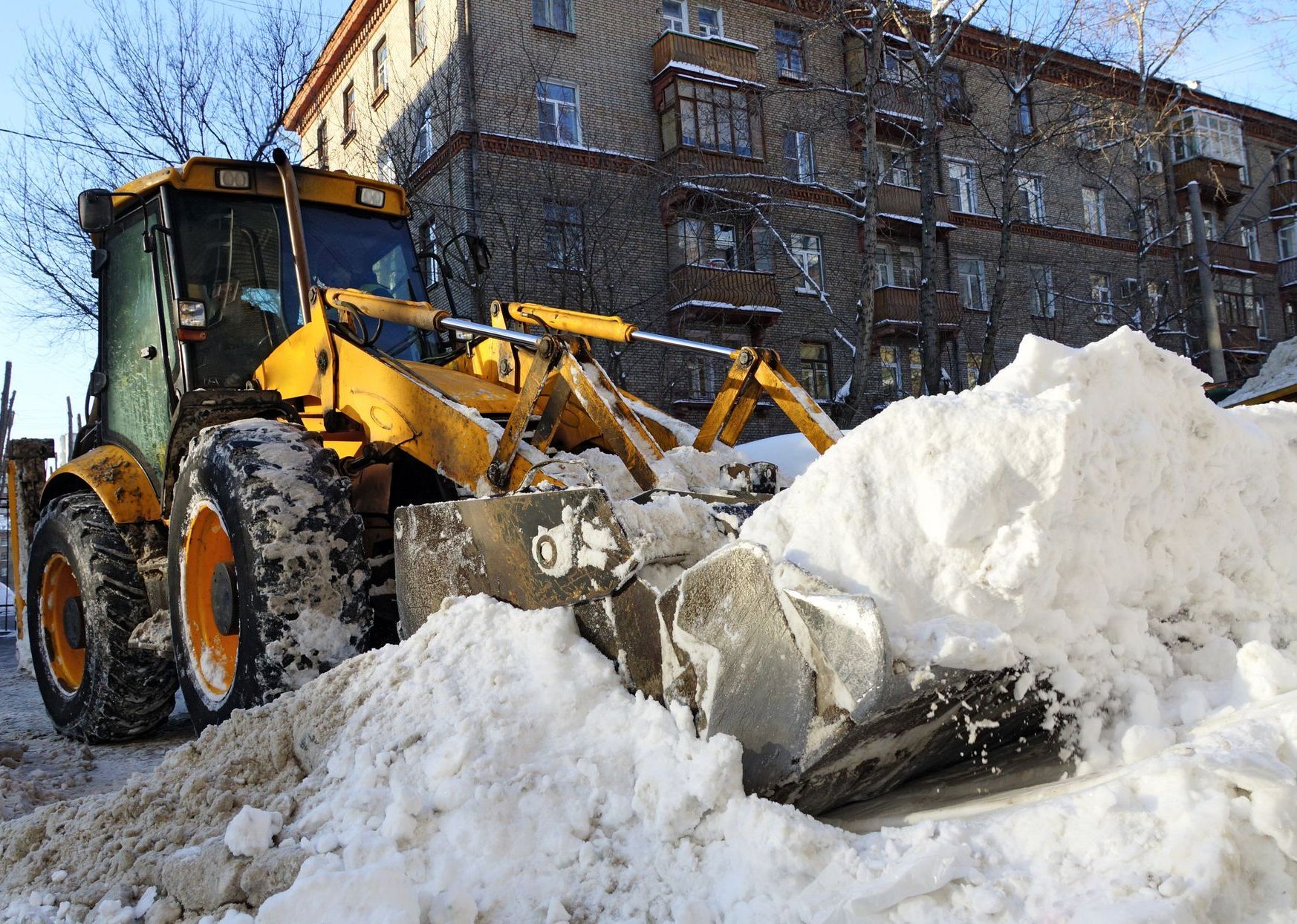 a yellow tractor is clearing snow in front of a building - professional snow removal