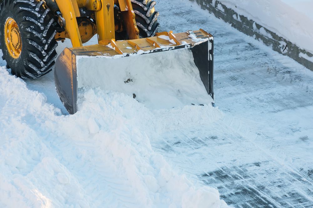 A yellow snow plow is clearing snow from the side of the road.