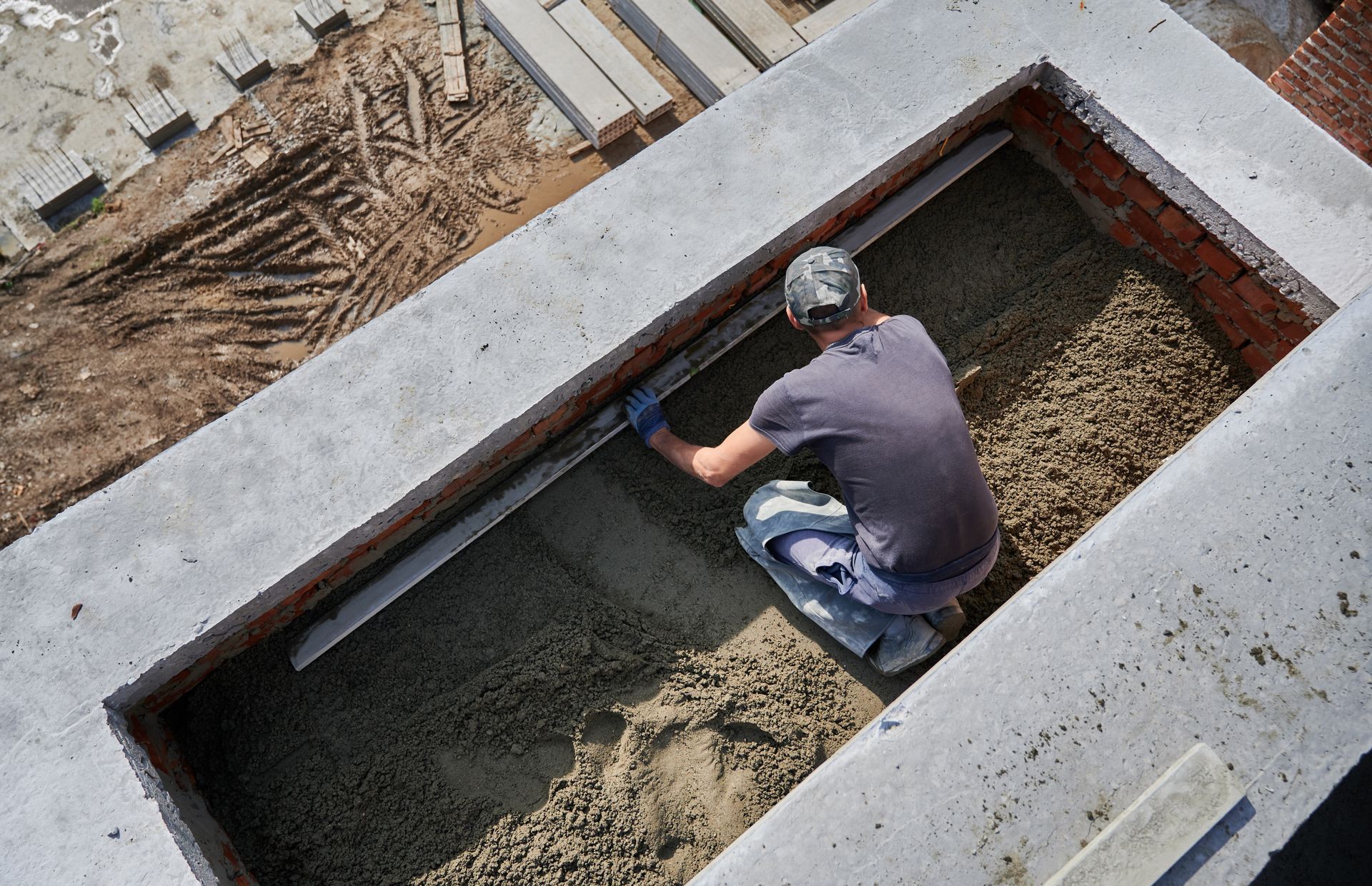 A man is kneeling in a hole in the ground using a level.