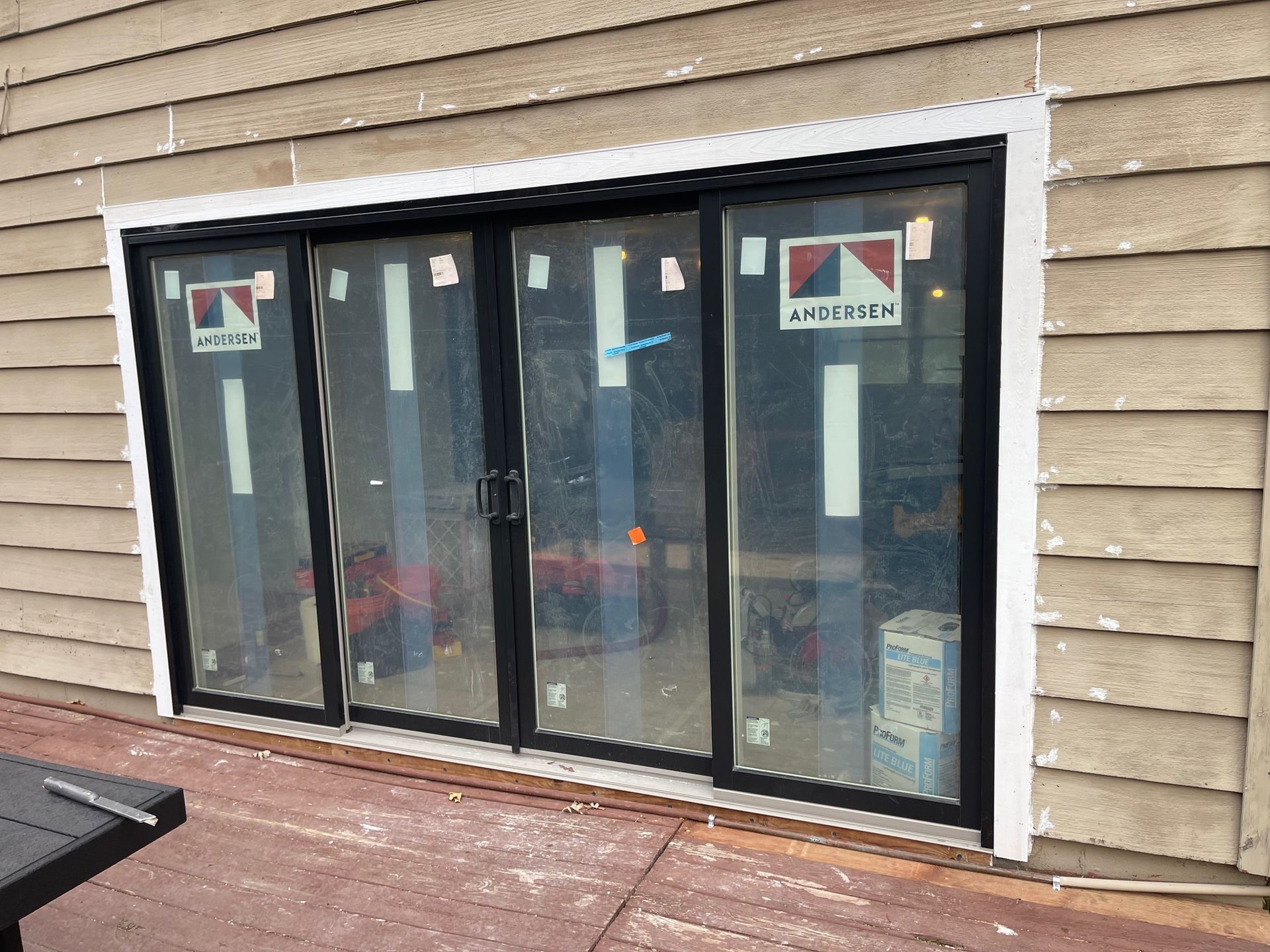 Sliding glass doors with black frames, white trim, and protective coverings. Installed on a wooden deck.