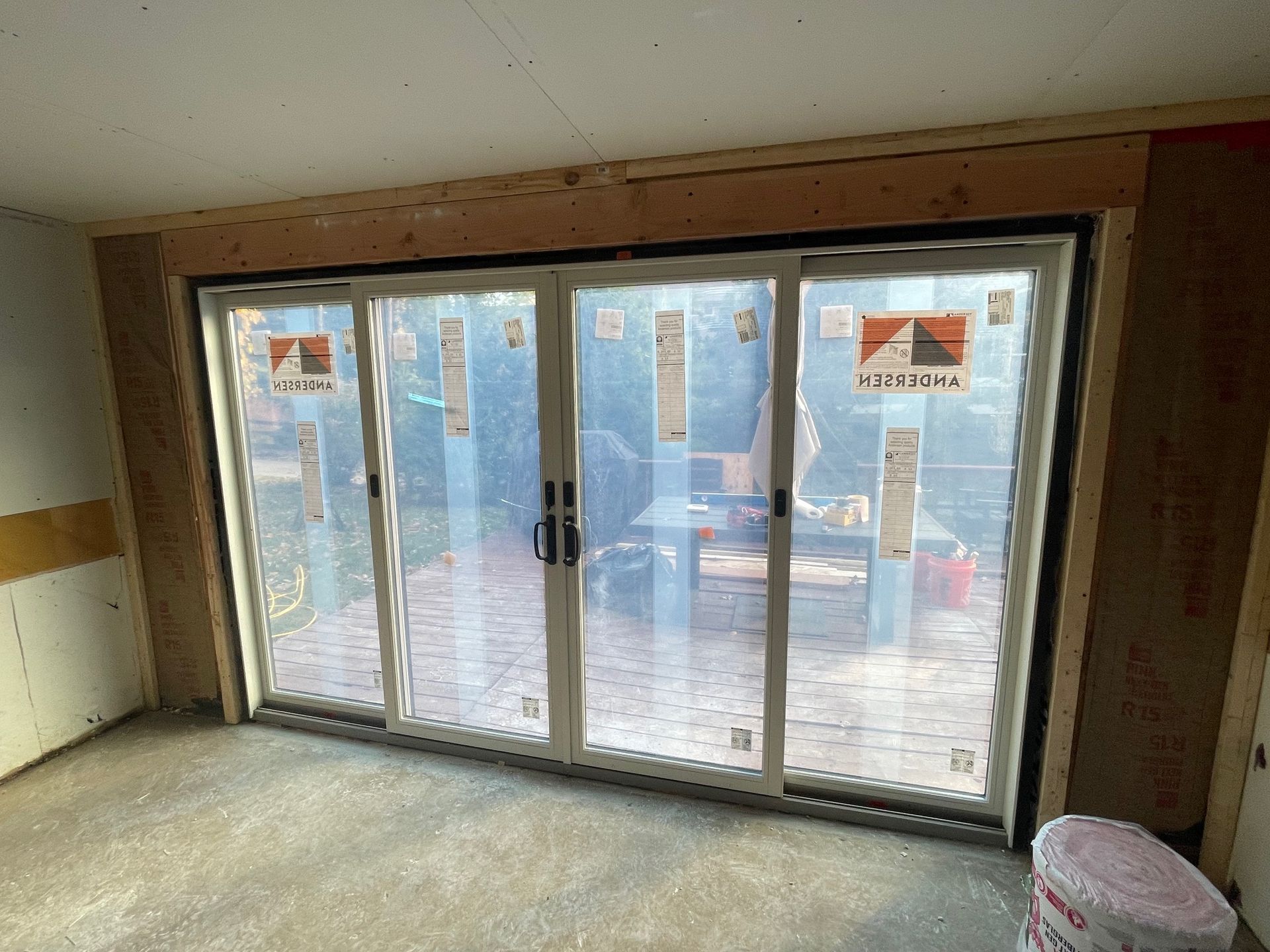 Sliding glass doors inside a room under construction, with visible wood framing and a bucket on the floor.