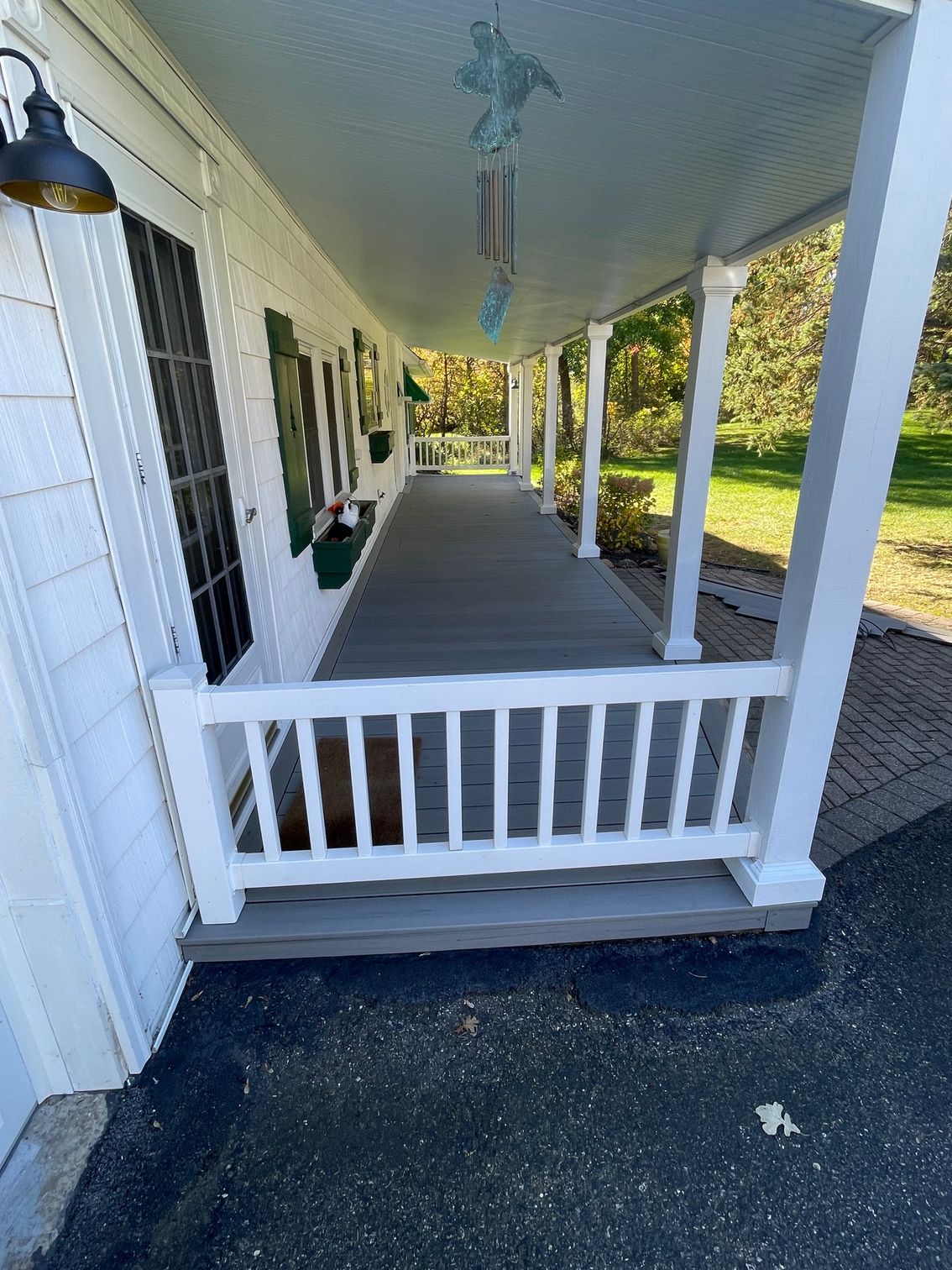 White porch with grey floor and railing, overhead light, overlooking a green lawn.