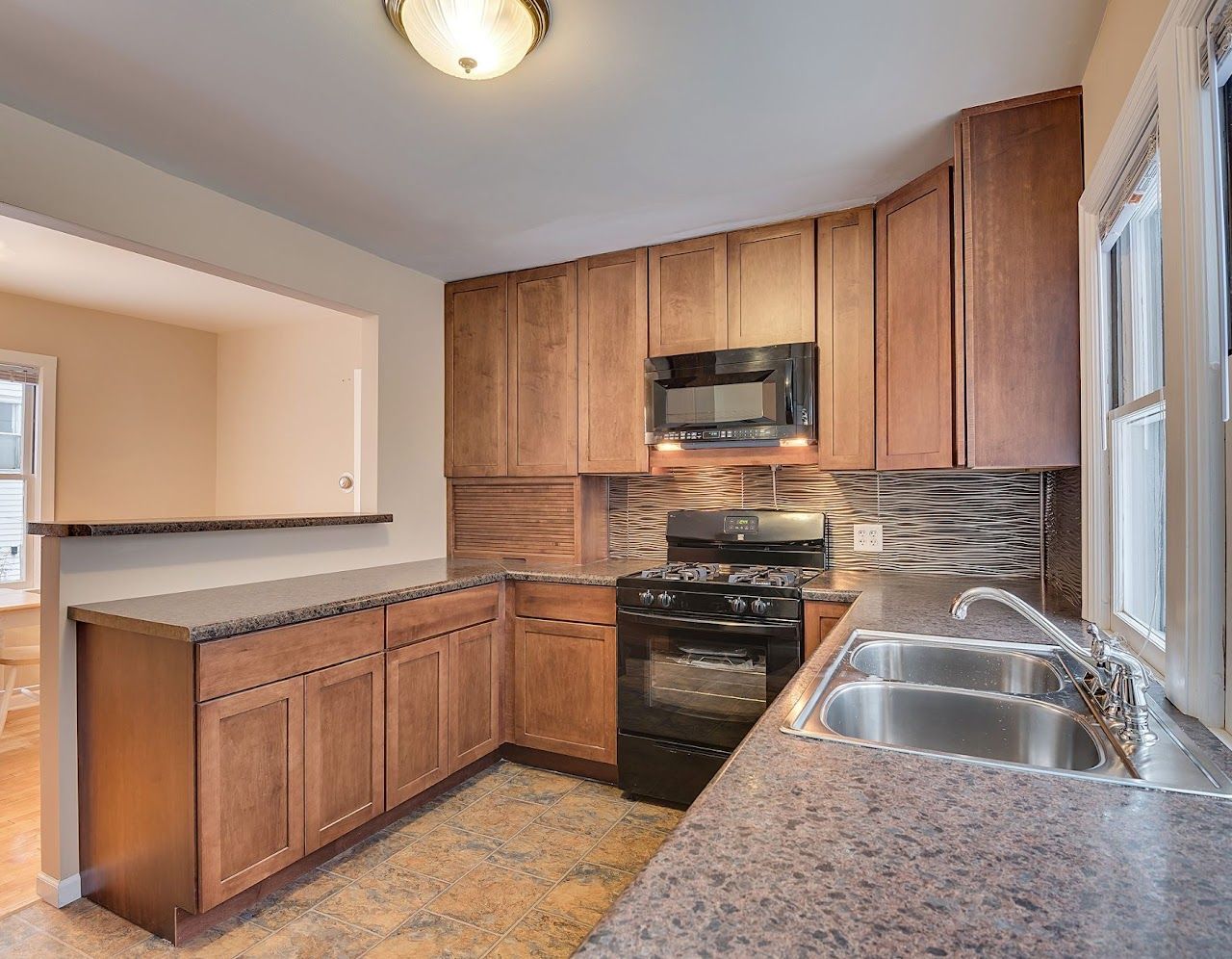 A kitchen with wooden cabinets, stainless steel appliances, a sink, stove and microwave.