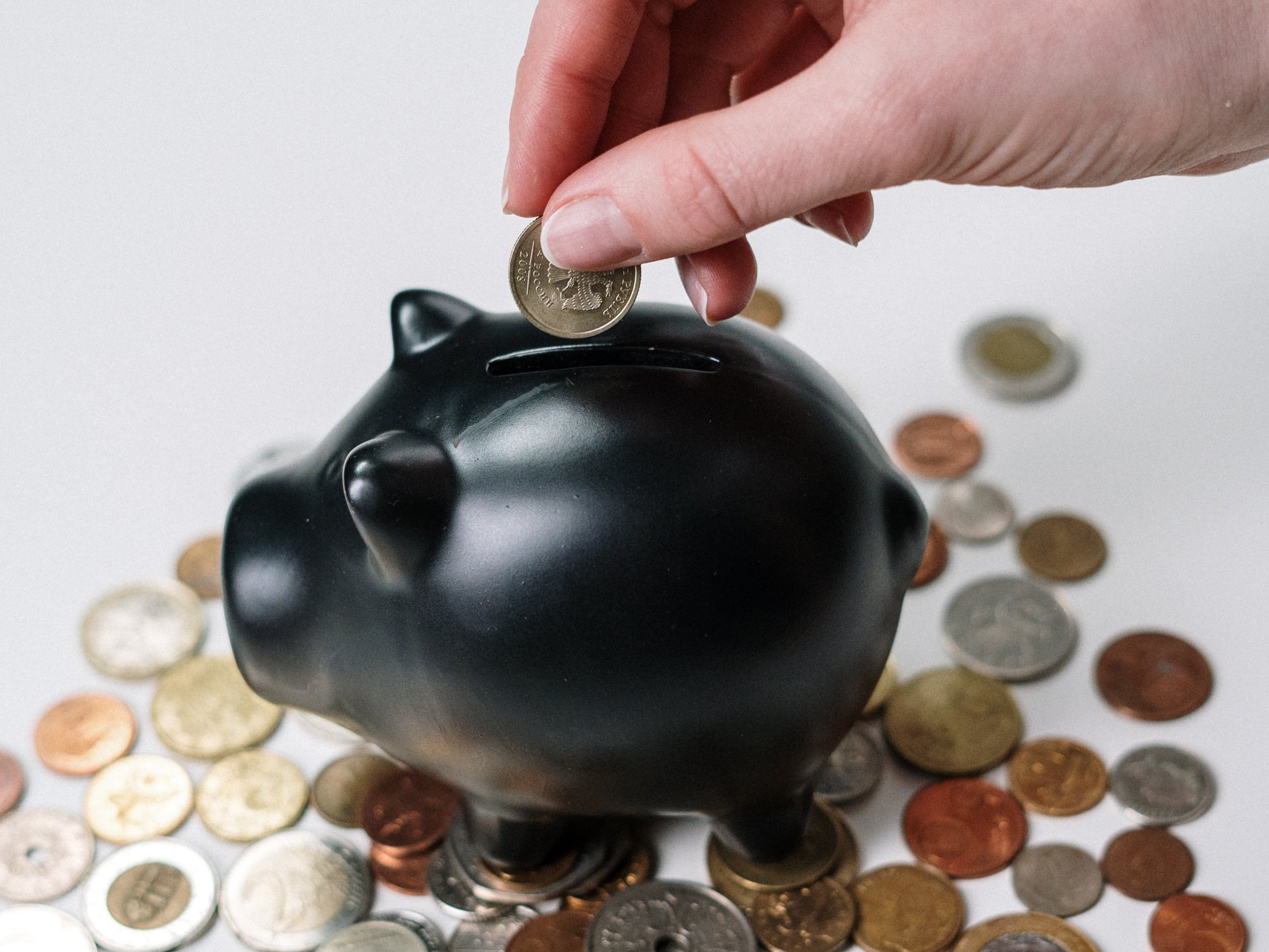 A person is putting a coin into a piggy bank surrounded by coins.
