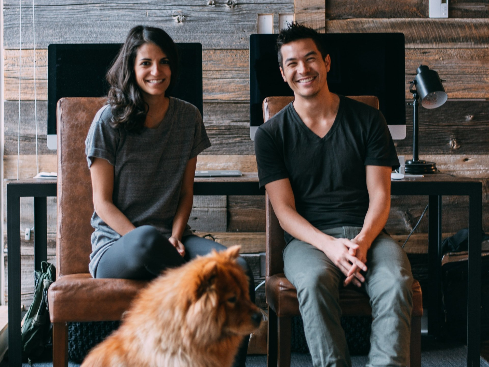 A man and a woman are sitting in chairs with a dog in front of them.