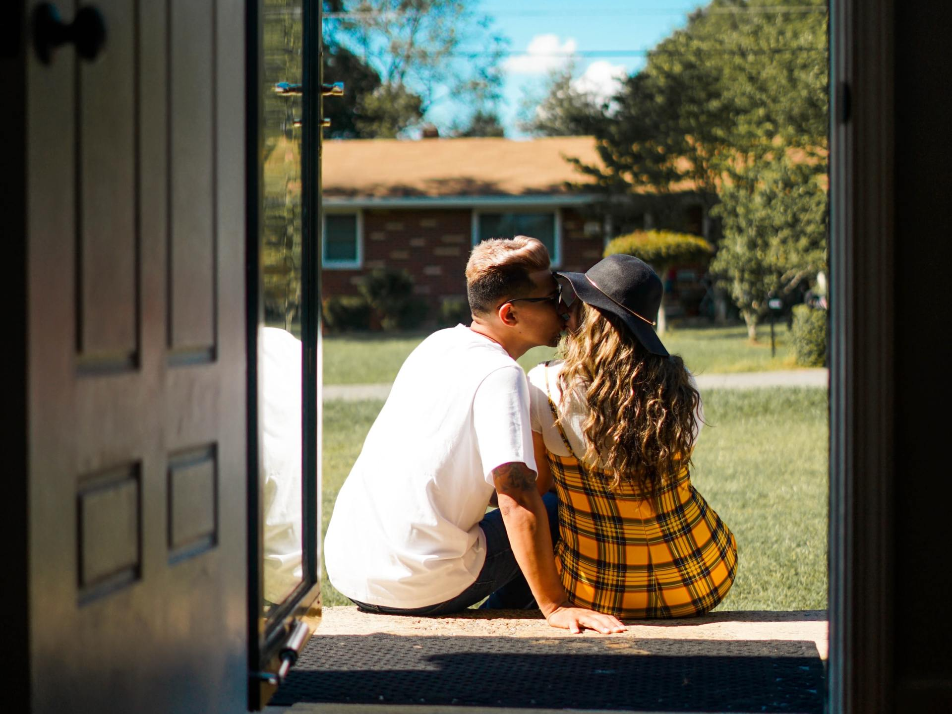 A man and a woman are kissing while sitting on the porch of a house.