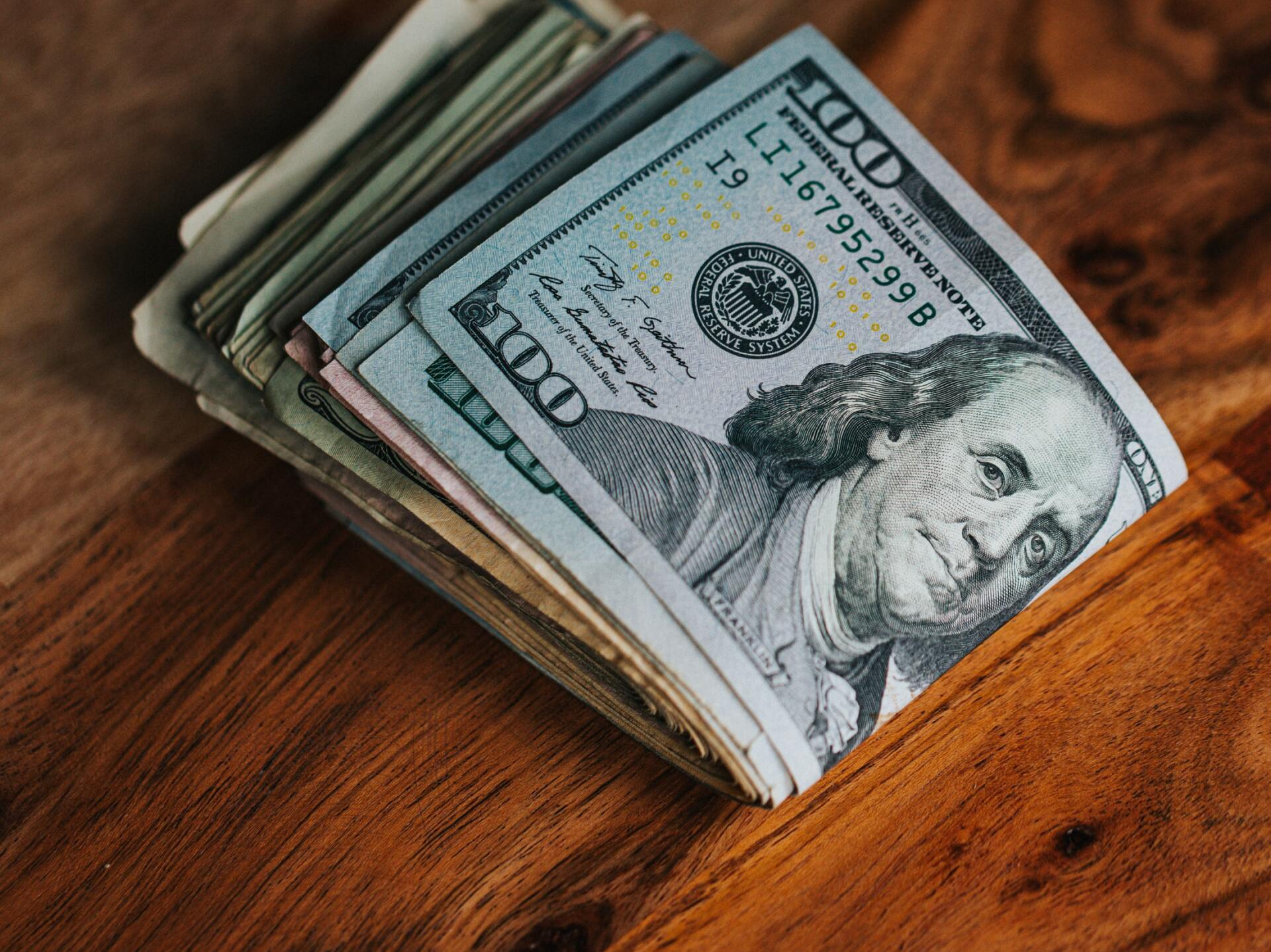 A stack of money is sitting on a wooden table.