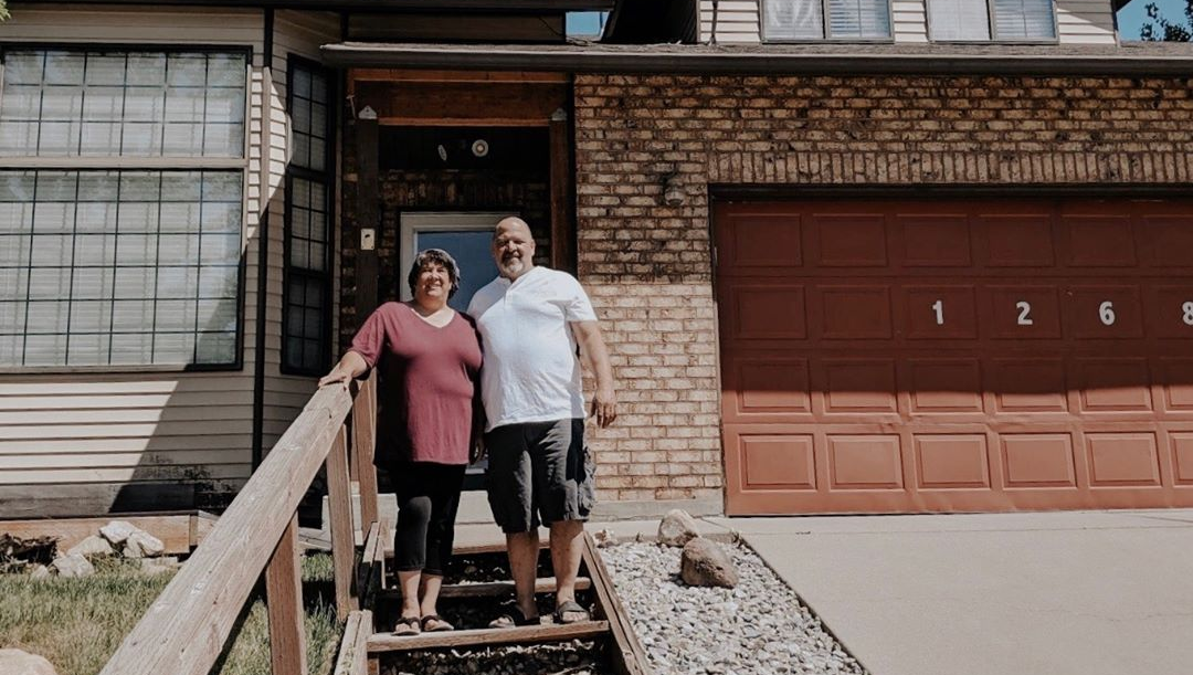 A man and a woman are standing in front of a house.