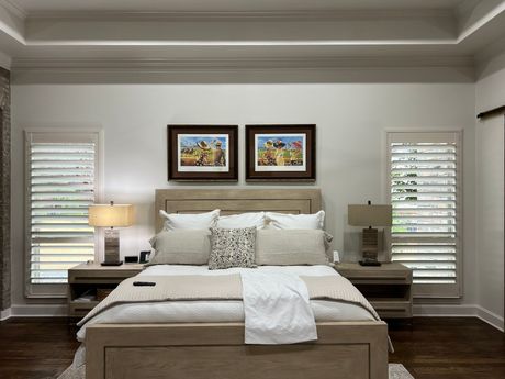 A bedroom with a king size bed , two nightstands , two lamps and two paintings on the wall.