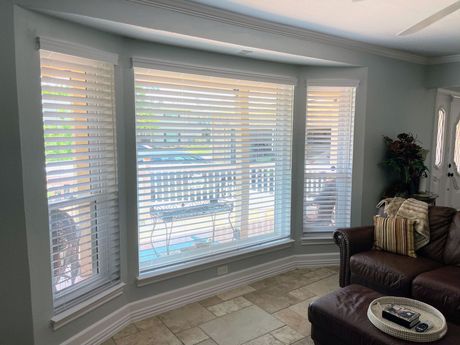 A living room with a couch , ottoman , and large windows with blinds.