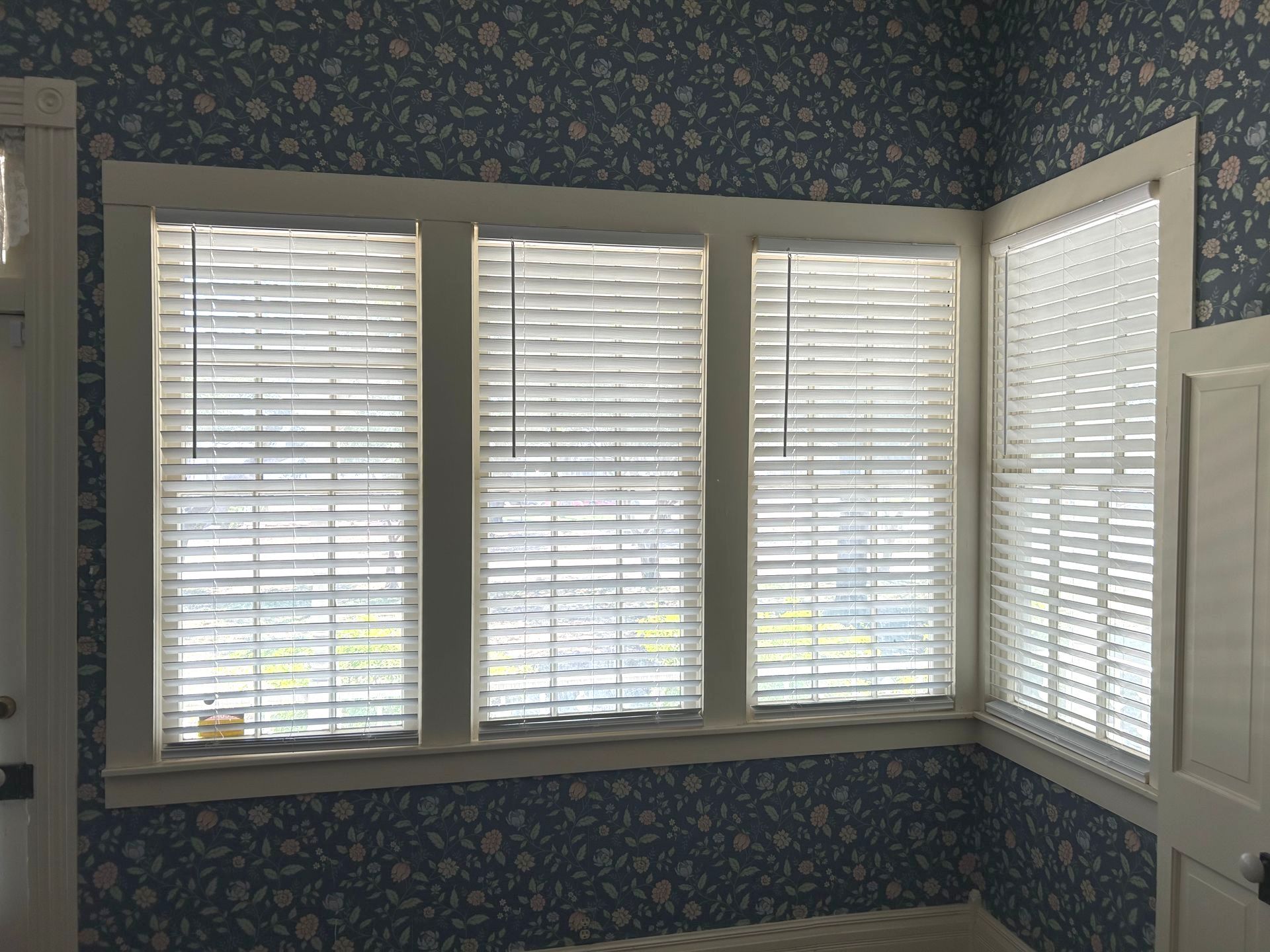 A room with blue floral wallpaper and white blinds on the windows.