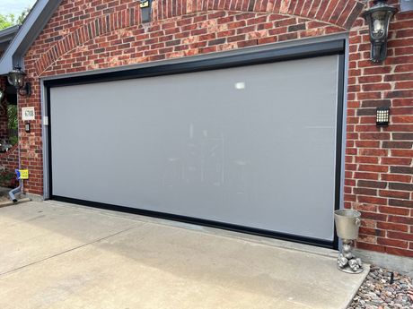 A gray garage door is sitting in front of a brick house.