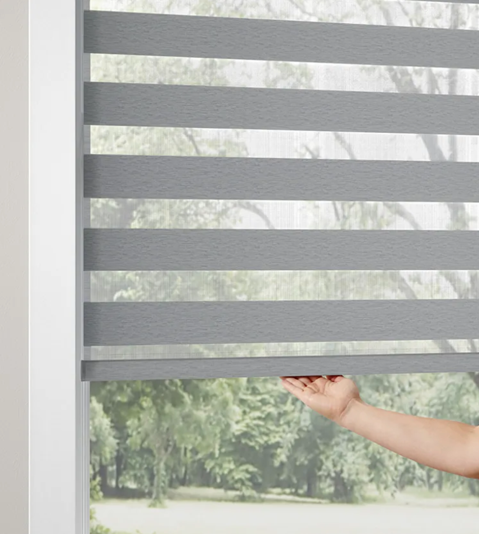 A person is opening a gray blind on a window.