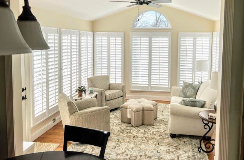A living room full of windows has white shutters and an arched window.