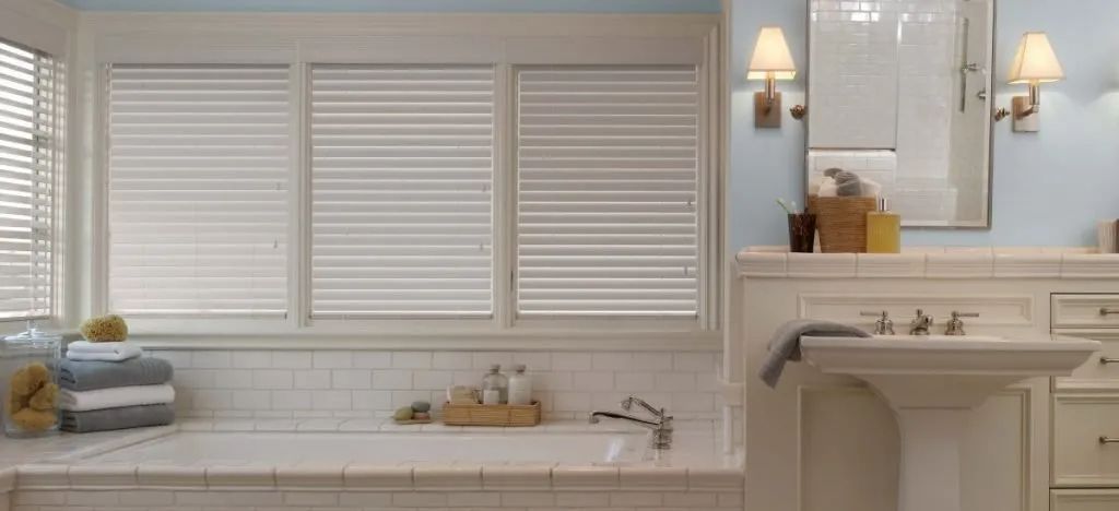 A bathroom with a tub , sink , mirror and eco-friendly blinds. Love is Blinds