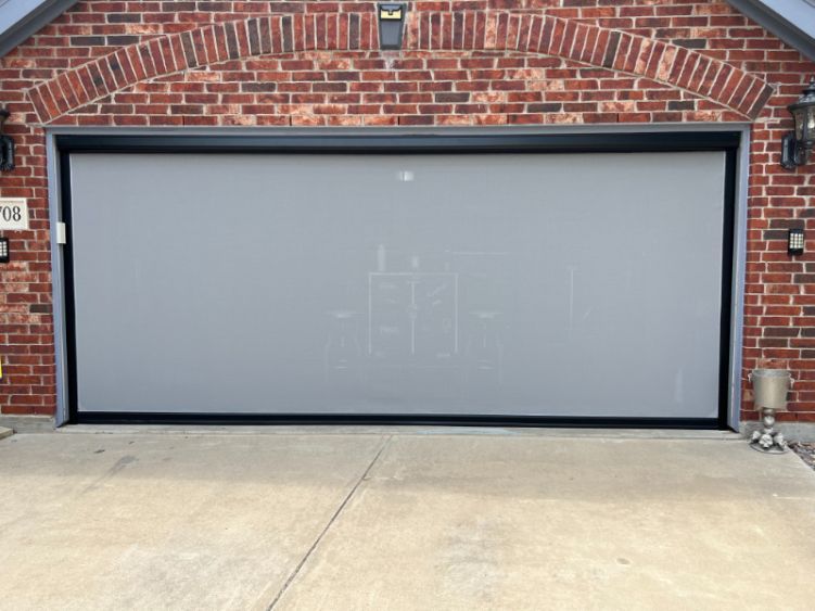 A red brick home has a garage with white exterior patio shades.