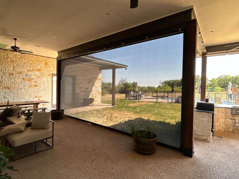 A living room with a couch , table , chairs and a screened in porch with motorized exterior patio shades. Love is Blinds