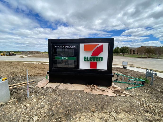 A 7 eleven sign is sitting in the middle of a dirt field.