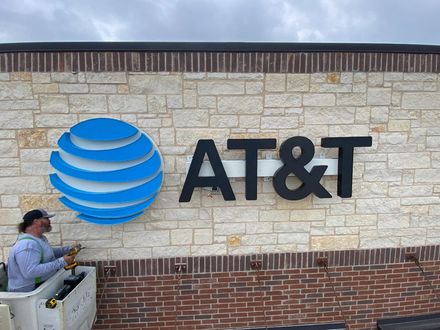 A man is painting a sign for at & t on a brick wall.