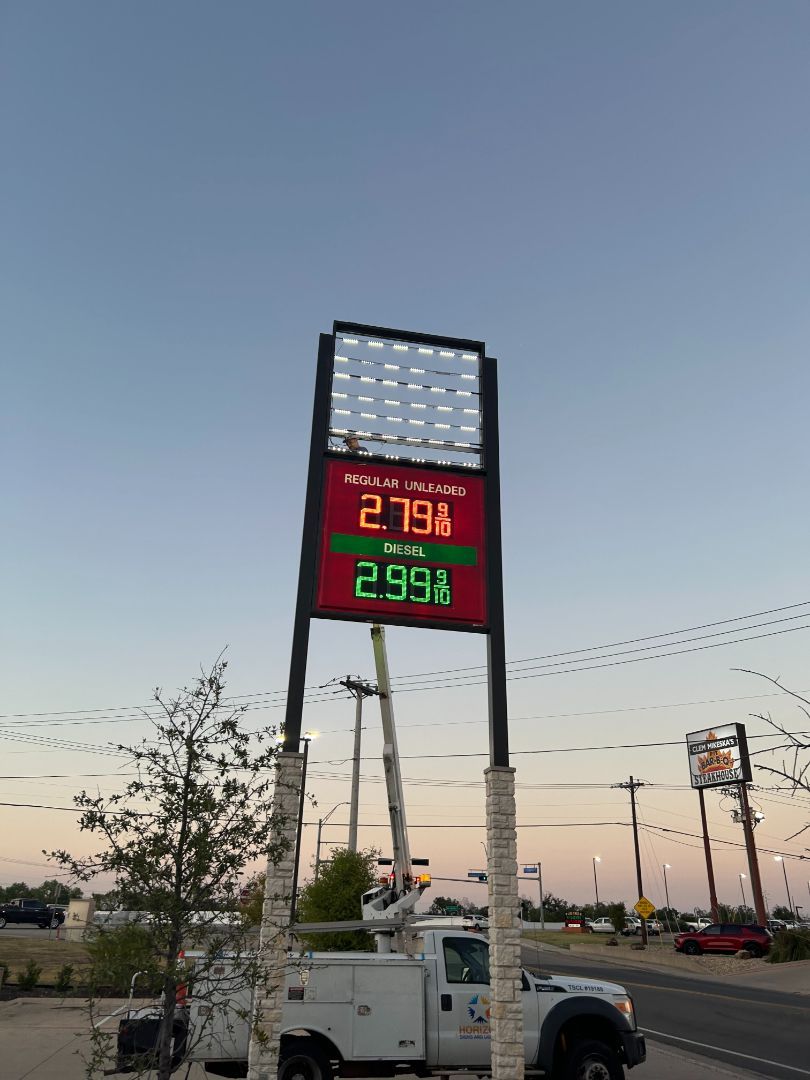 A white truck is parked in front of a gas station sign.