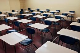 Empty classroom with rows of blue chairs and white desks on a maroon floor.
