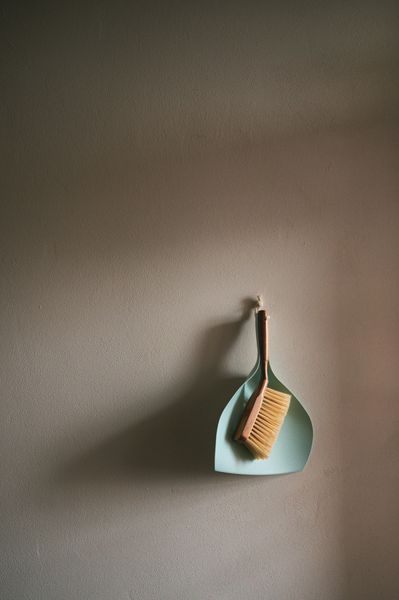 Dustpan and brush hanging on a textured wall, casting a shadow.