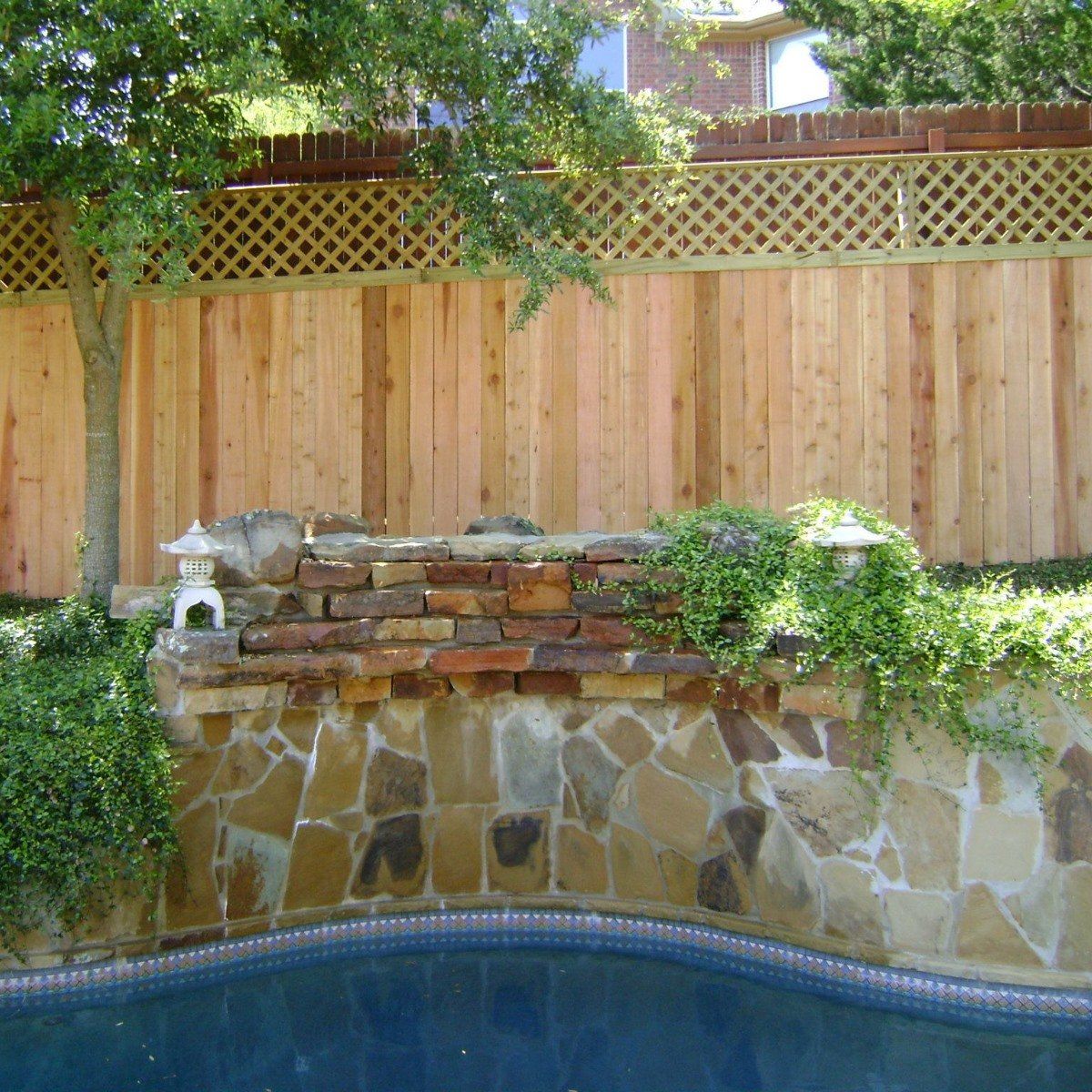 A wooden fence surrounds a stone wall next to a swimming pool