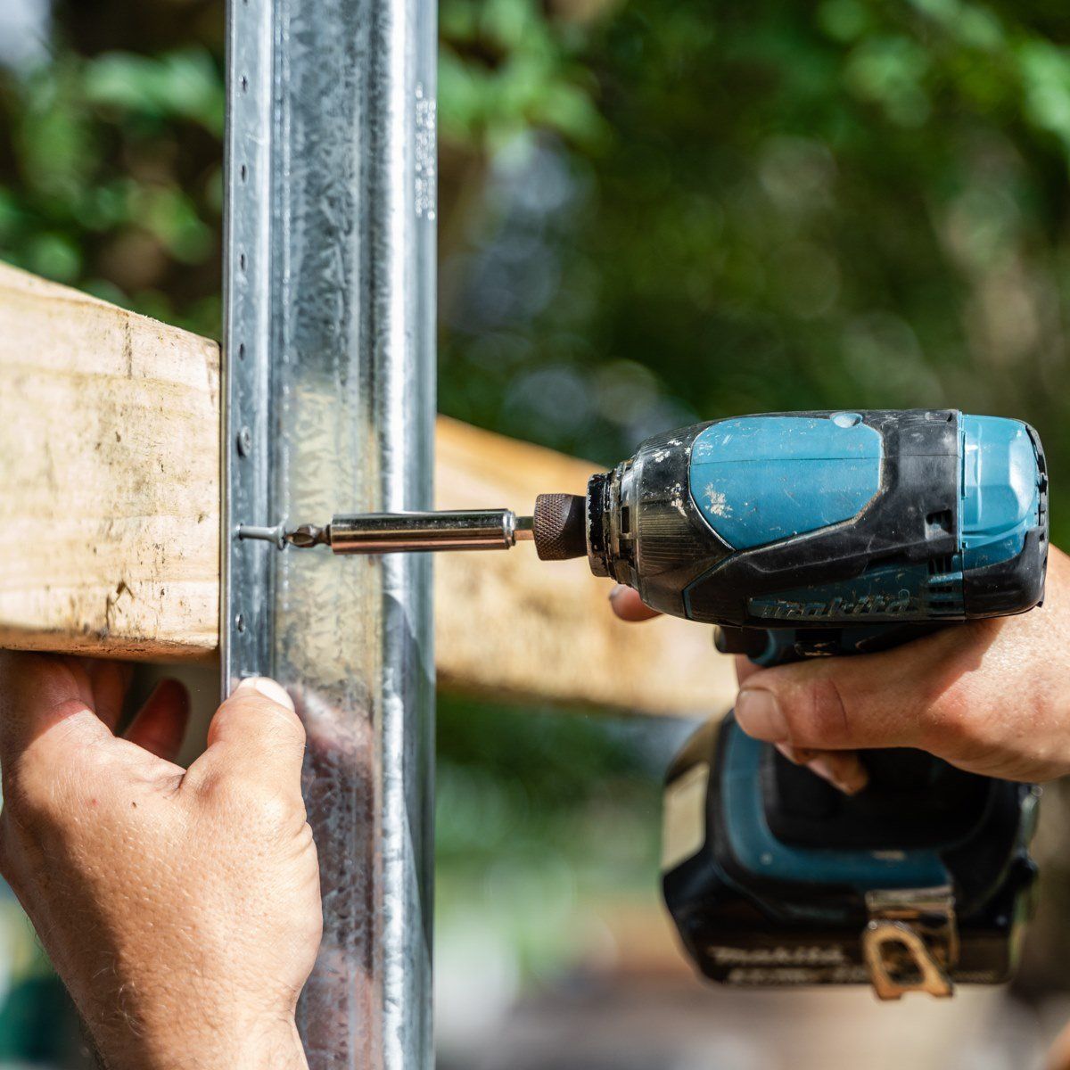 A person is using a drill to screw a screw into a metal post.