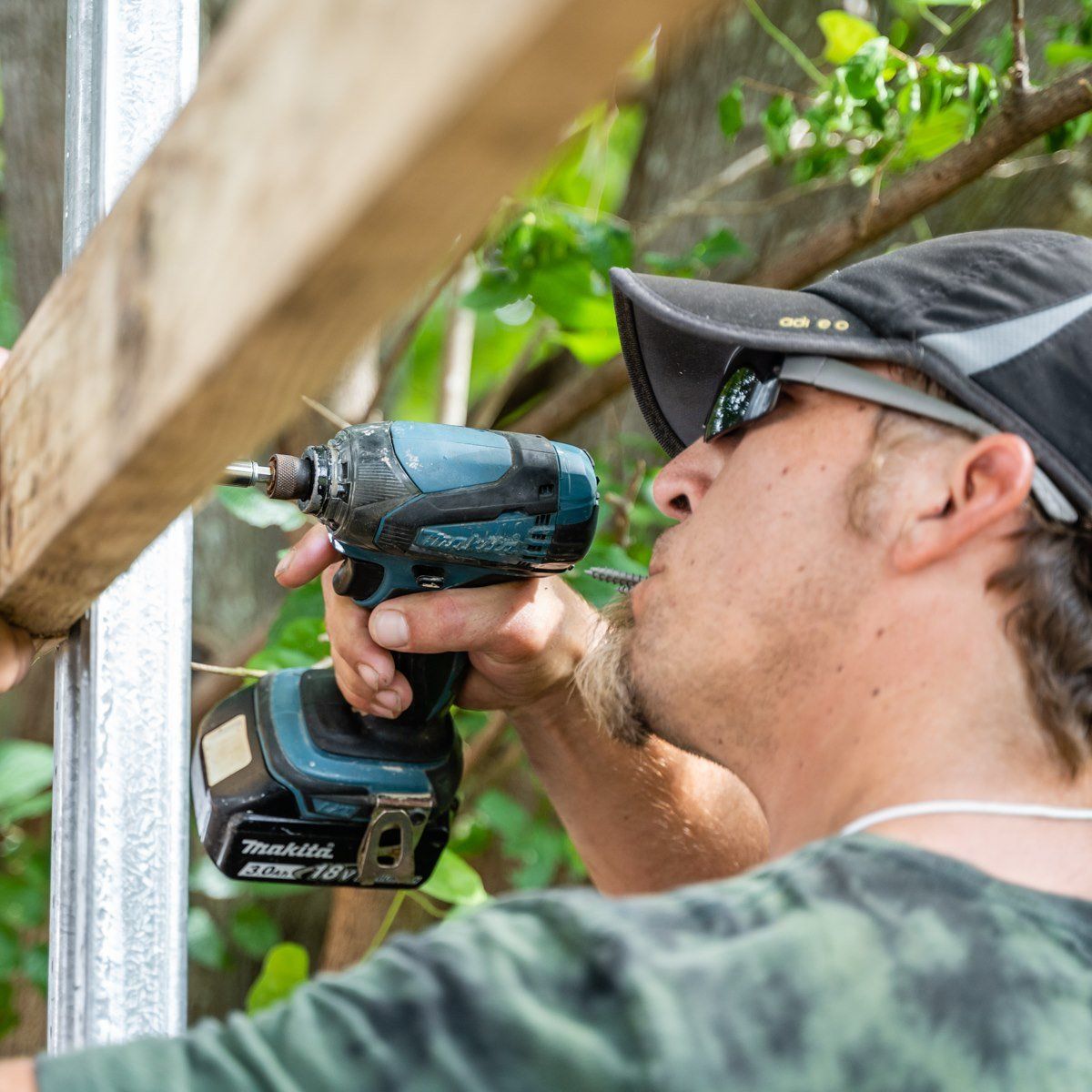 A man is using a makita drill on a wooden post.