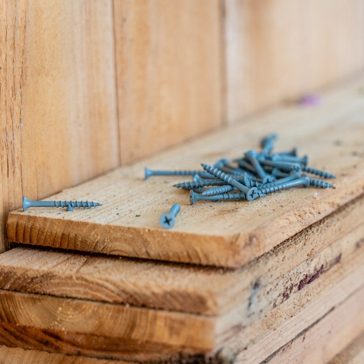 A bunch of screws are sitting on top of a wooden plank.
