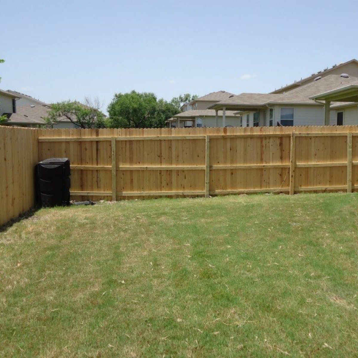 A wooden fence surrounds a lush green lawn in a backyard.