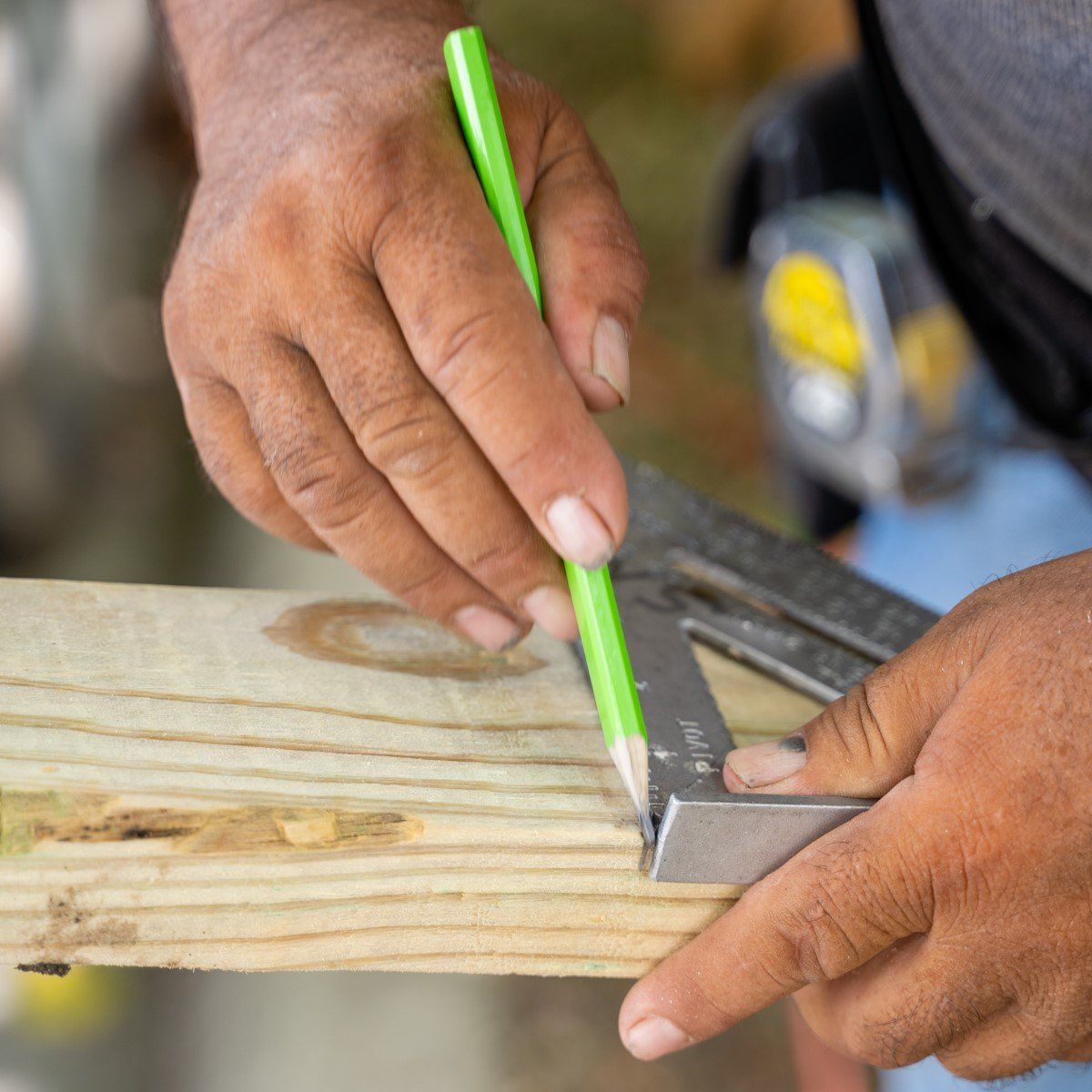 A man is measuring a piece of wood with a green pencil