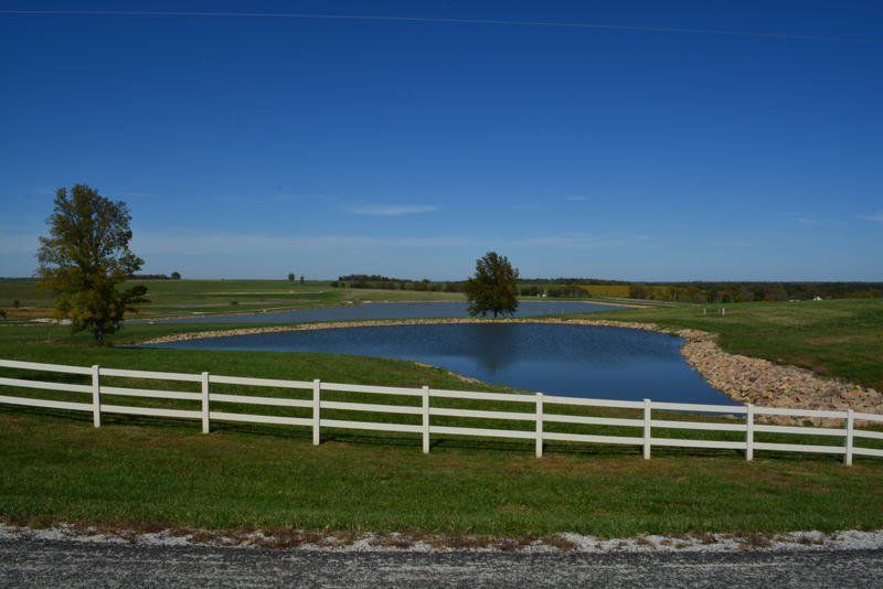 A white fence surrounds a pond in a grassy field